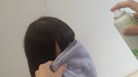 前髪にスプレーが付かないようにタオルを使っている写真