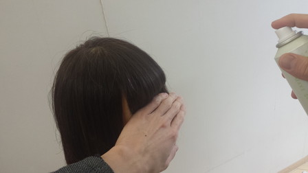 前髪にスプレーがつかないように手で防いでいる写真