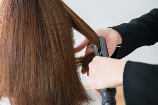 ヘアアイロンする美容師の写真