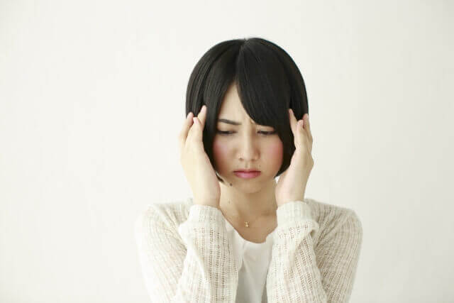 頭に手を当てて困る女性の写真