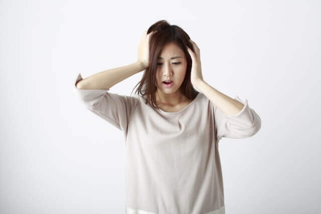 頭に手を当て悩む女性の写真