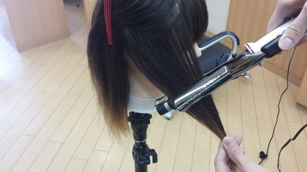 髪の毛をコテで巻いている写真